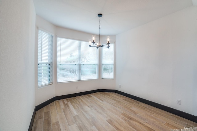 empty room with a notable chandelier and light hardwood / wood-style floors