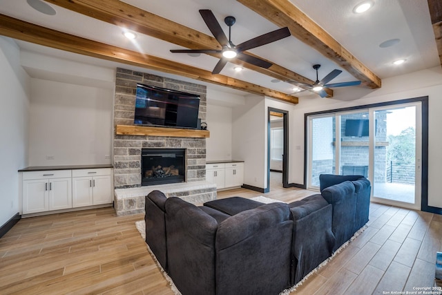 living room with ceiling fan, a stone fireplace, and beamed ceiling