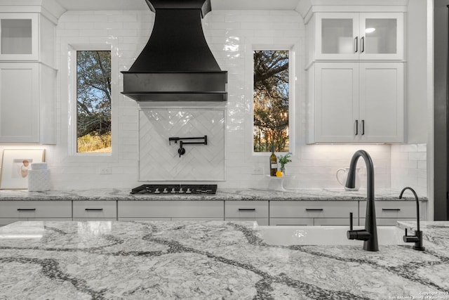 kitchen featuring custom exhaust hood, light stone countertops, stainless steel gas cooktop, and white cabinets