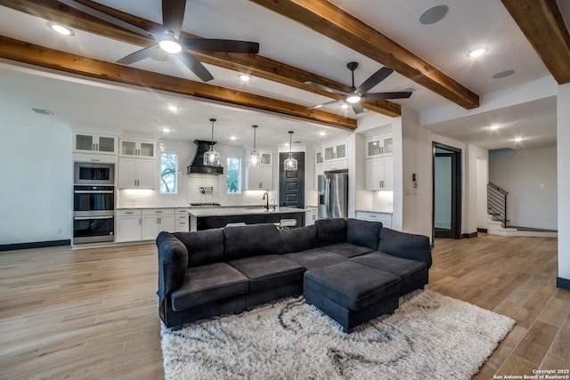 living room with beamed ceiling, sink, ceiling fan, and light hardwood / wood-style flooring