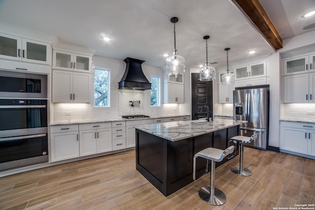 kitchen featuring premium range hood, a breakfast bar, white cabinetry, stainless steel appliances, and a kitchen island with sink