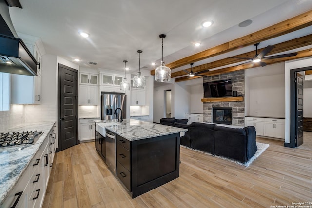 kitchen with appliances with stainless steel finishes, a stone fireplace, pendant lighting, white cabinetry, and a kitchen island with sink