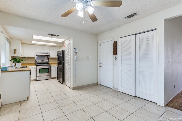 kitchen featuring stainless steel electric range oven, light tile patterned flooring, white cabinetry, black fridge, and a textured ceiling