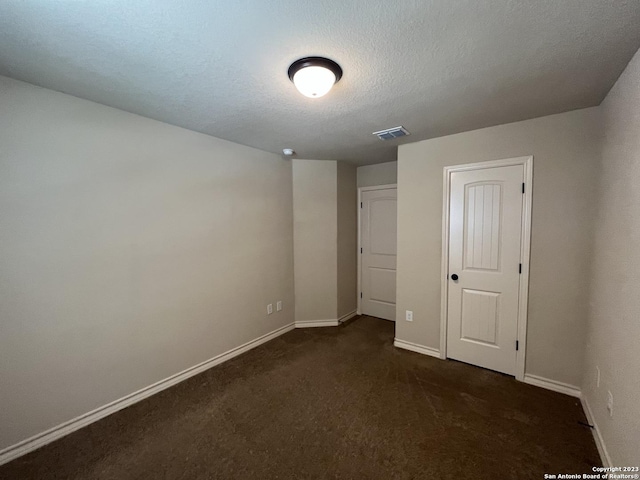 unfurnished bedroom with a textured ceiling and dark carpet