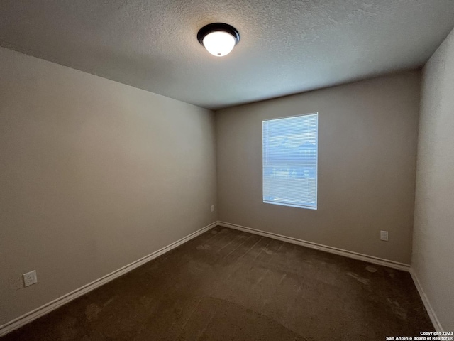 spare room featuring a textured ceiling and dark colored carpet