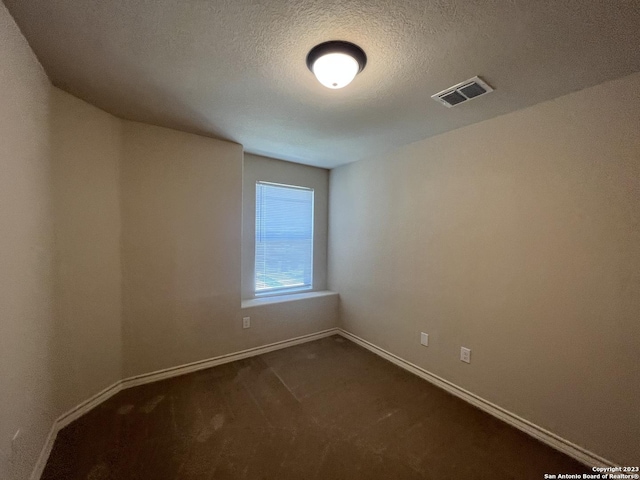 unfurnished room featuring a textured ceiling and dark carpet