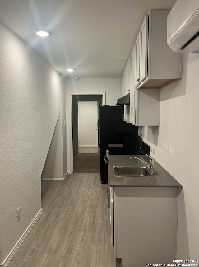 kitchen with black refrigerator, a wall mounted AC, light wood-type flooring, sink, and white cabinetry