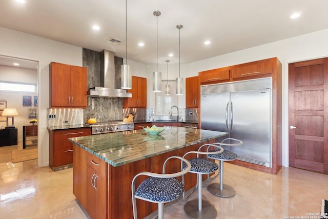 kitchen featuring hanging light fixtures, stainless steel built in refrigerator, a center island, and wall chimney exhaust hood