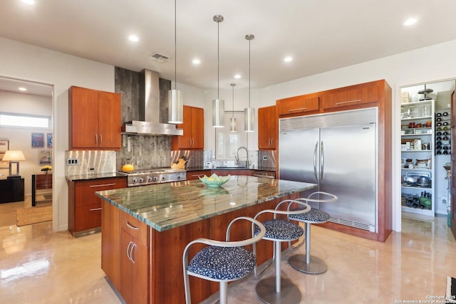 kitchen with built in refrigerator, decorative light fixtures, wall chimney exhaust hood, and a kitchen island