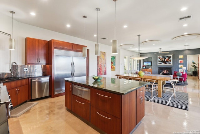 kitchen featuring appliances with stainless steel finishes, a center island, tasteful backsplash, decorative light fixtures, and sink