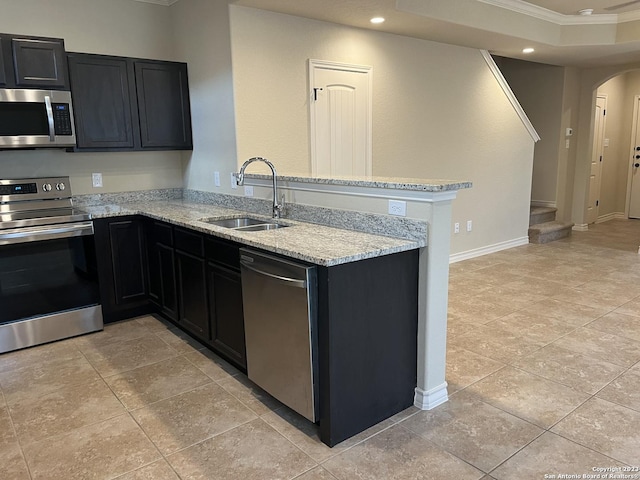 kitchen with appliances with stainless steel finishes, kitchen peninsula, ornamental molding, light stone counters, and sink