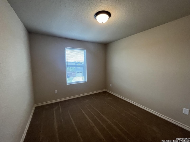 empty room featuring a textured ceiling and dark colored carpet