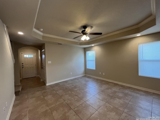 empty room with a raised ceiling, ceiling fan, crown molding, and light tile patterned floors