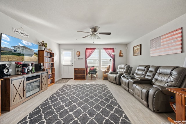 living room with light wood-type flooring, ceiling fan, and a textured ceiling