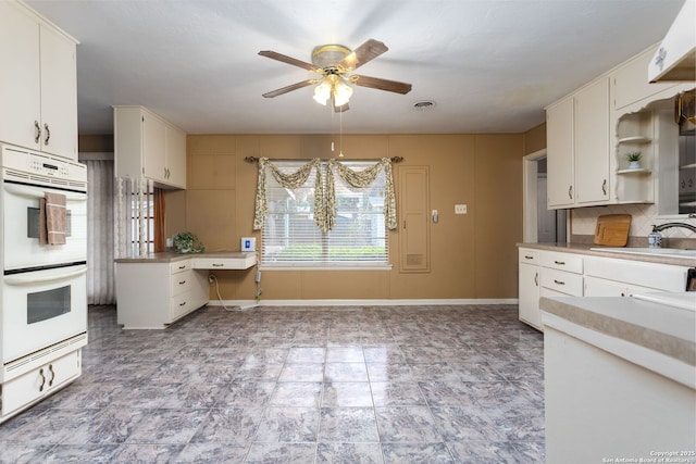 kitchen with white double oven, backsplash, white cabinetry, ceiling fan, and sink