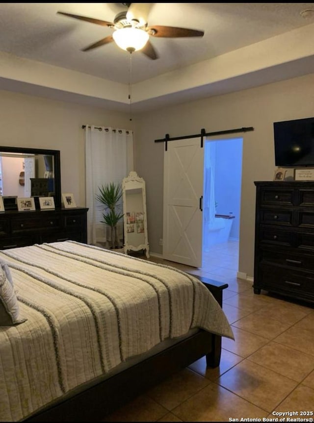 tiled bedroom featuring a raised ceiling, a barn door, and ceiling fan