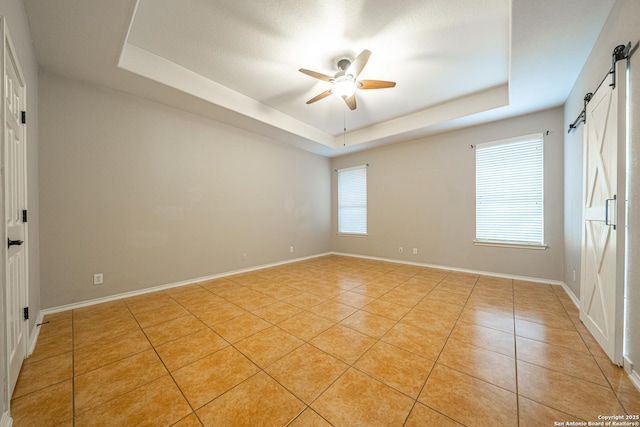 spare room with a tray ceiling, a barn door, ceiling fan, and light tile patterned flooring