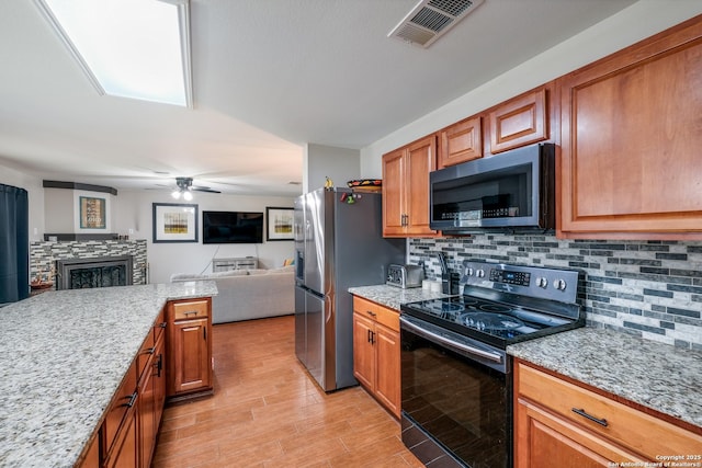 kitchen featuring a stone fireplace, stainless steel appliances, ceiling fan, light stone counters, and backsplash