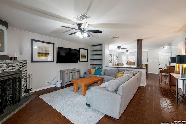 living room with ornate columns, a fireplace, ceiling fan, and dark wood-type flooring