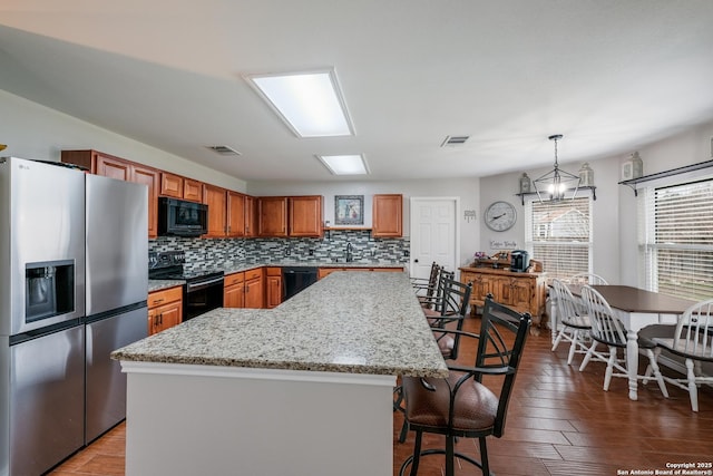 kitchen with black appliances, a center island, a healthy amount of sunlight, and decorative light fixtures