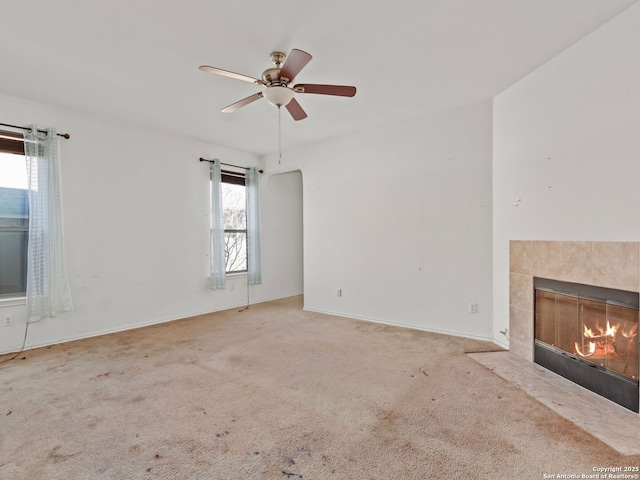 unfurnished living room with ceiling fan, a wealth of natural light, a tile fireplace, and light carpet