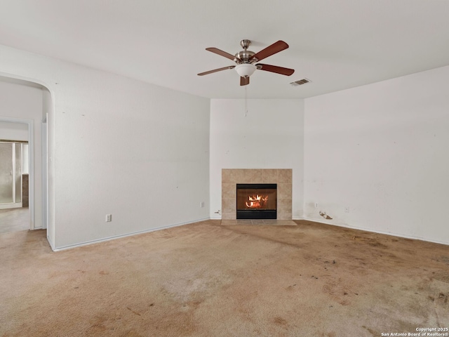 unfurnished living room with a tile fireplace, carpet floors, and ceiling fan