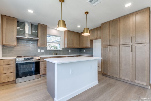 kitchen featuring stainless steel electric stove, decorative light fixtures, a center island, light hardwood / wood-style floors, and wall chimney range hood