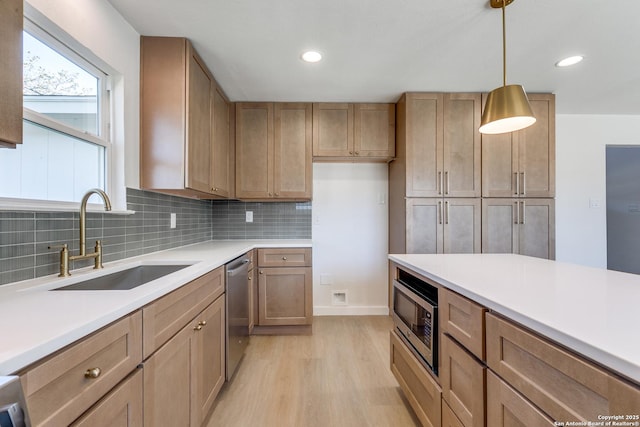 kitchen with appliances with stainless steel finishes, pendant lighting, sink, light hardwood / wood-style flooring, and tasteful backsplash