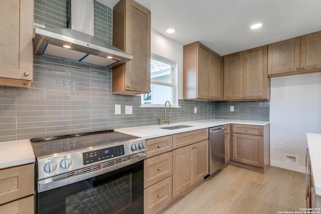 kitchen featuring stainless steel appliances, sink, light hardwood / wood-style floors, backsplash, and wall chimney range hood