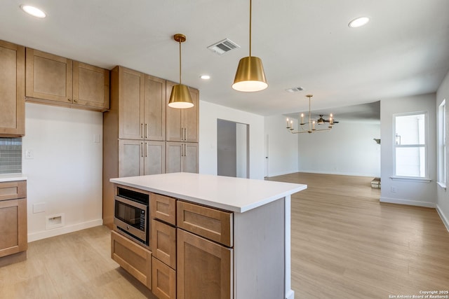 kitchen with light wood-type flooring, decorative light fixtures, an inviting chandelier, and stainless steel microwave