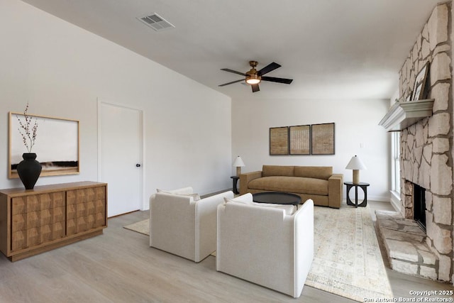 living room featuring ceiling fan, light hardwood / wood-style flooring, a stone fireplace, and vaulted ceiling