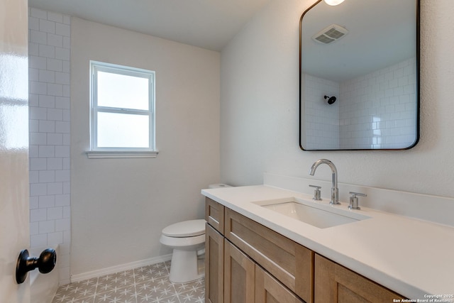 bathroom with toilet, tiled shower, and vanity