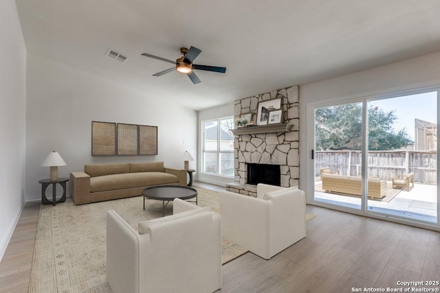 living room featuring ceiling fan, light hardwood / wood-style flooring, a wealth of natural light, and a stone fireplace