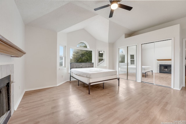 unfurnished bedroom featuring a tile fireplace, vaulted ceiling, ceiling fan, two closets, and light hardwood / wood-style flooring