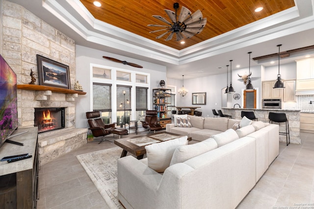 living room with wooden ceiling, a towering ceiling, a raised ceiling, crown molding, and a stone fireplace