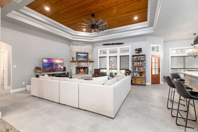 living room with wood ceiling, a fireplace, ceiling fan with notable chandelier, and a tray ceiling