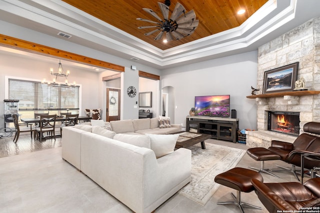 living room with wooden ceiling, ornamental molding, a fireplace, a tray ceiling, and ceiling fan with notable chandelier