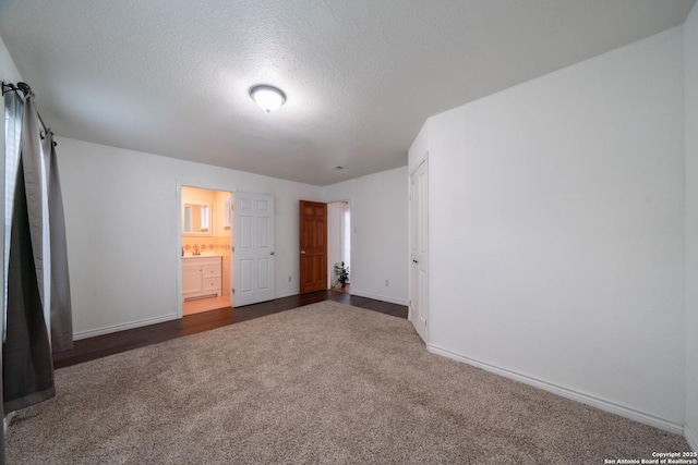 unfurnished bedroom featuring ensuite bathroom, dark carpet, and a textured ceiling