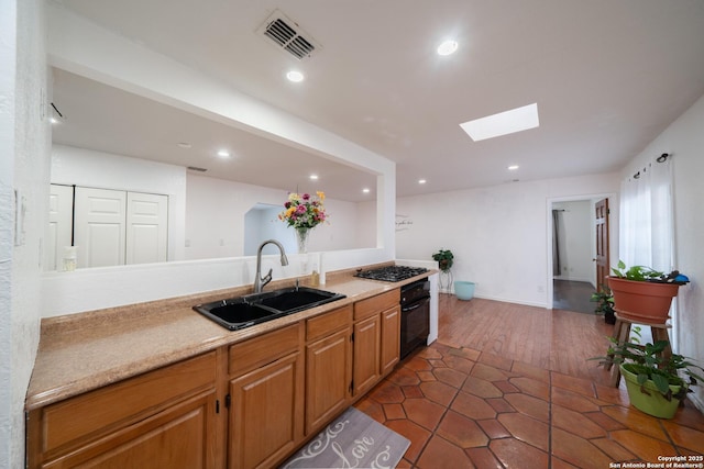 kitchen featuring sink, black oven, stainless steel gas stovetop, a skylight, and dark tile patterned floors