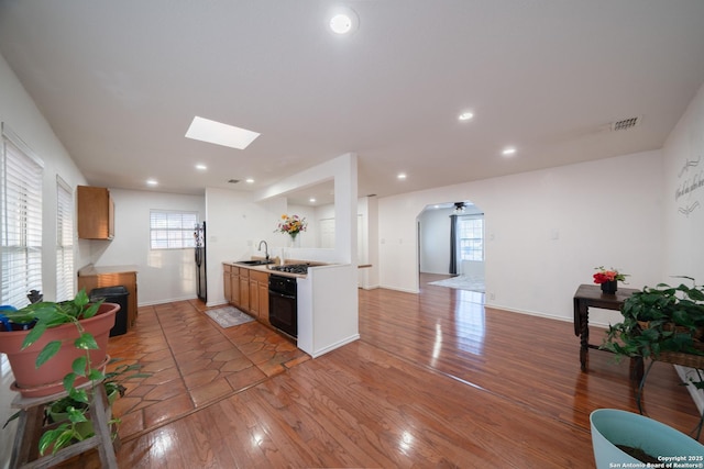 kitchen with black refrigerator, oven, a skylight, wood-type flooring, and sink