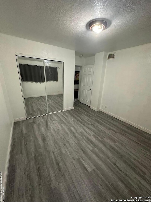 unfurnished bedroom with a textured ceiling, a closet, and dark hardwood / wood-style floors