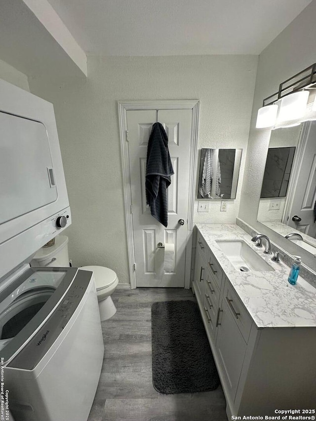 bathroom featuring toilet, vanity, stacked washer and clothes dryer, and hardwood / wood-style floors