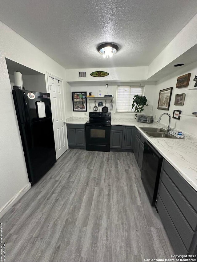 kitchen featuring light stone counters, a textured ceiling, black appliances, gray cabinetry, and sink