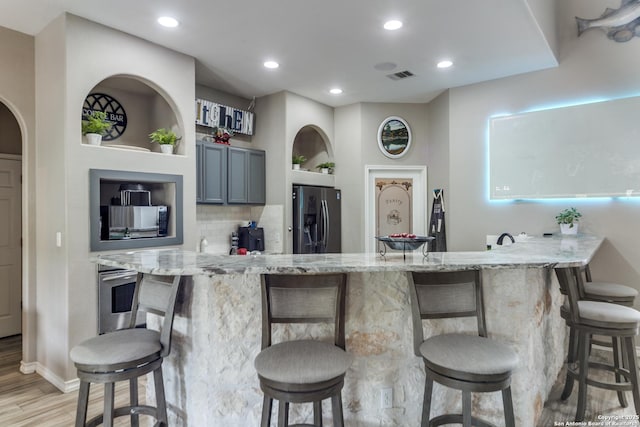 kitchen featuring light stone counters, a kitchen bar, appliances with stainless steel finishes, gray cabinetry, and built in features