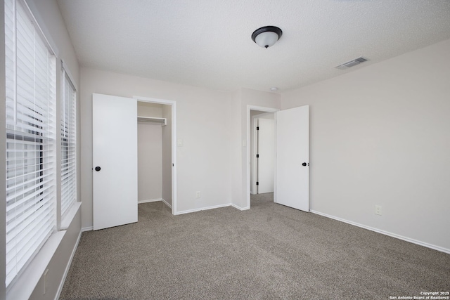 unfurnished bedroom with a closet, carpet, a spacious closet, multiple windows, and a textured ceiling