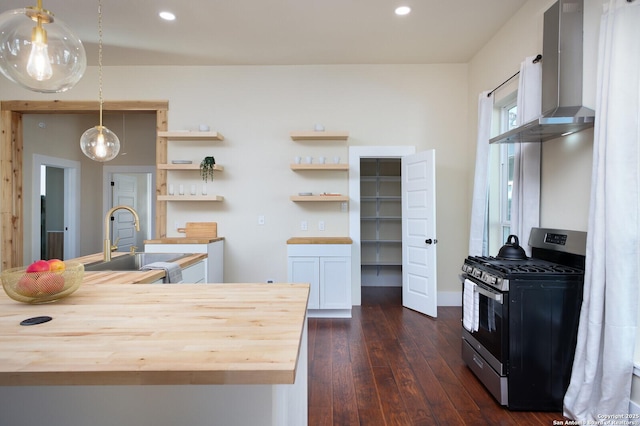 kitchen with sink, decorative light fixtures, wall chimney exhaust hood, butcher block countertops, and gas range