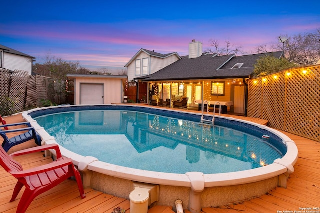 pool at dusk featuring a deck and an outbuilding