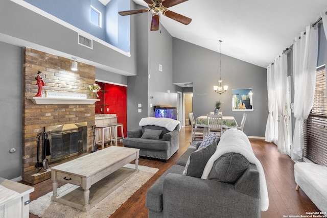 living room featuring ceiling fan with notable chandelier, high vaulted ceiling, a fireplace, and dark wood-type flooring