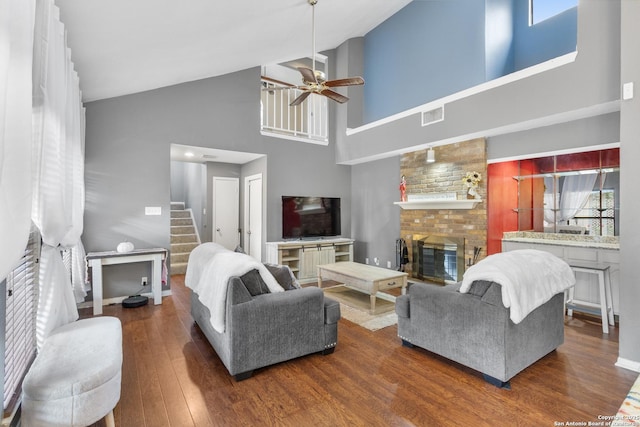 living room with a towering ceiling, a fireplace, dark wood-type flooring, and ceiling fan