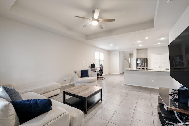 tiled living room with ceiling fan and a tray ceiling